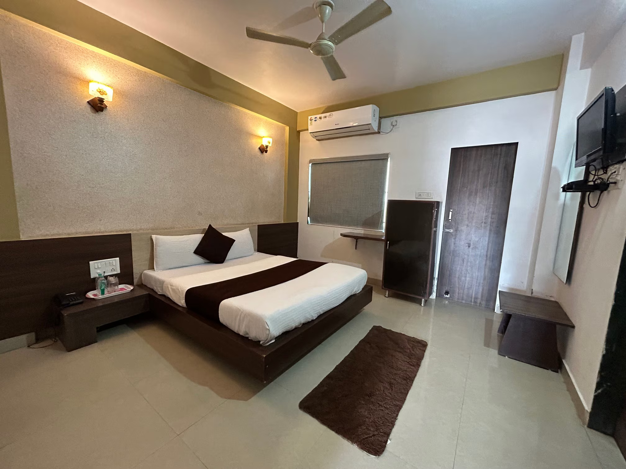 Hotel Somnath Atithigruh's double AC room featuring a TV, bedside tables, and ample lighting for guest comfort.